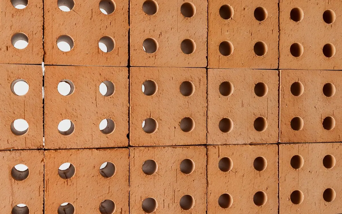 Muro de ladrillos de terracota natural con cuatro agujeros cada uno, algunos pasantes que dejan ver la luz