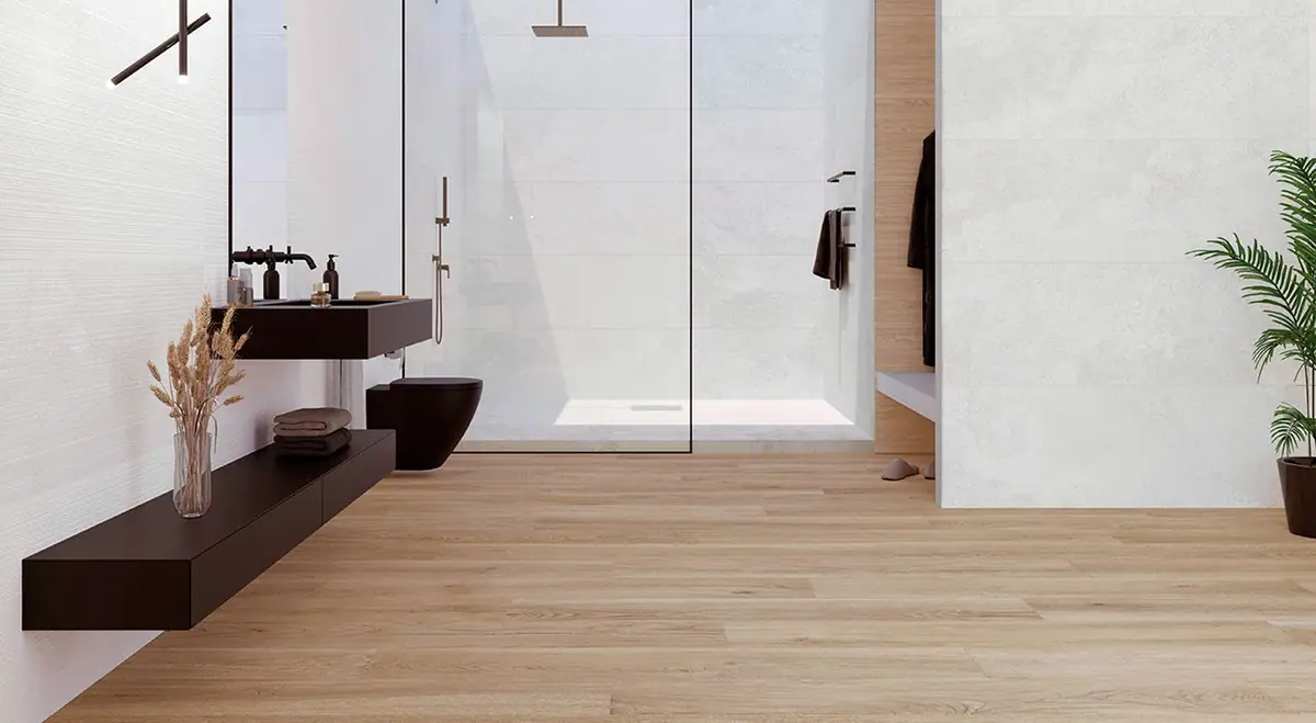 Baño con paredes blancas de efecto piedra, una de ellas con relieve de líneas, mueble de lavabo oscuro y suelo de madera