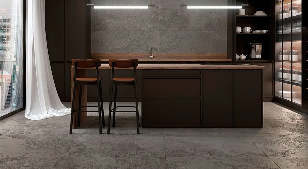 Cocina con isla oscura, taburetes de madera y suelo y pared de porcelánico efecto piedra gris