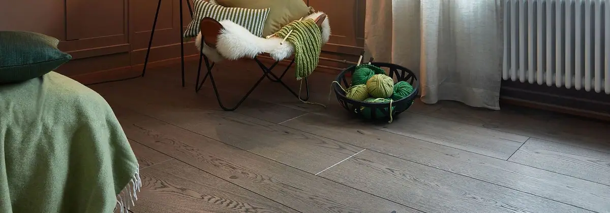 Dormitorio con suelo de tablones de roble en tono oscuro, butaca con manta y cesta de ovillos de lana