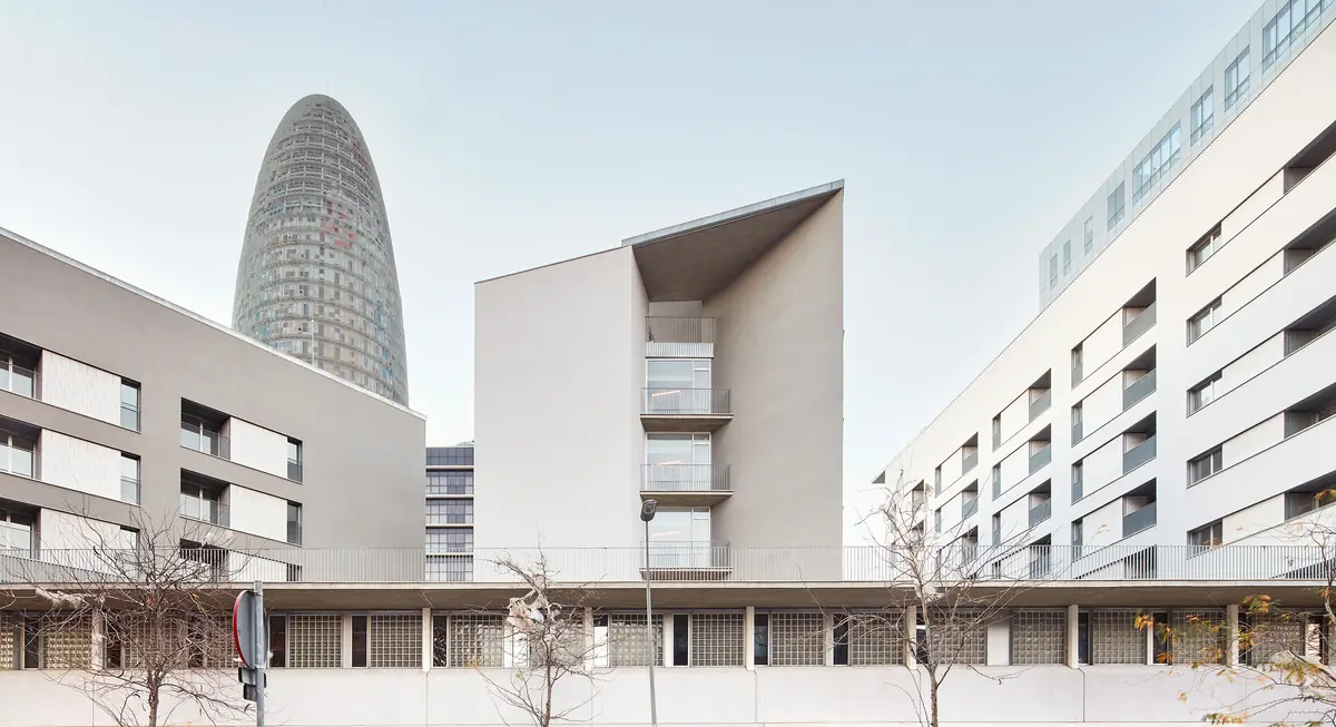 Tres bloques de viviendas blancos sobre un basamento común, con la torre Glòries al fondo