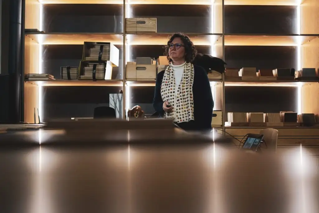 Una de las arquitectas invitadas, con pañuelo de lunares, escucha de pie ante las estanterías iluminadas de Matter Barcelona