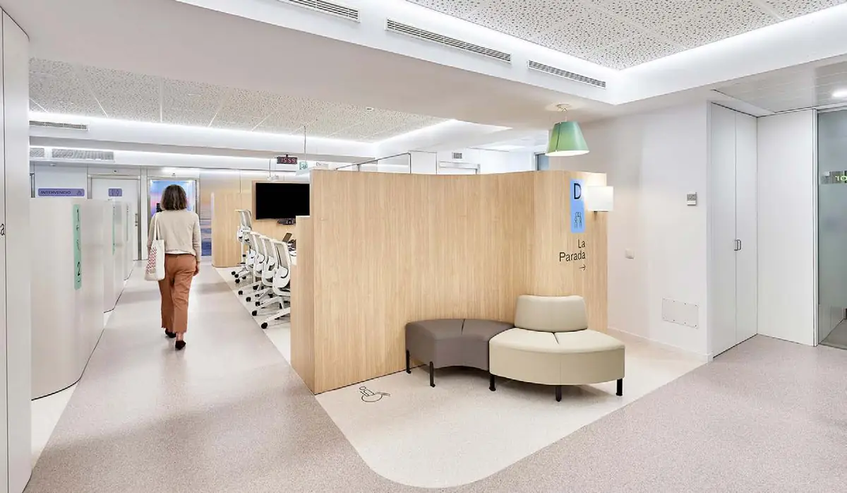 Pasillo de una unidad hospitalaria con revestimientos de madera clara, asientos curvos y suelo con formas redondeadas