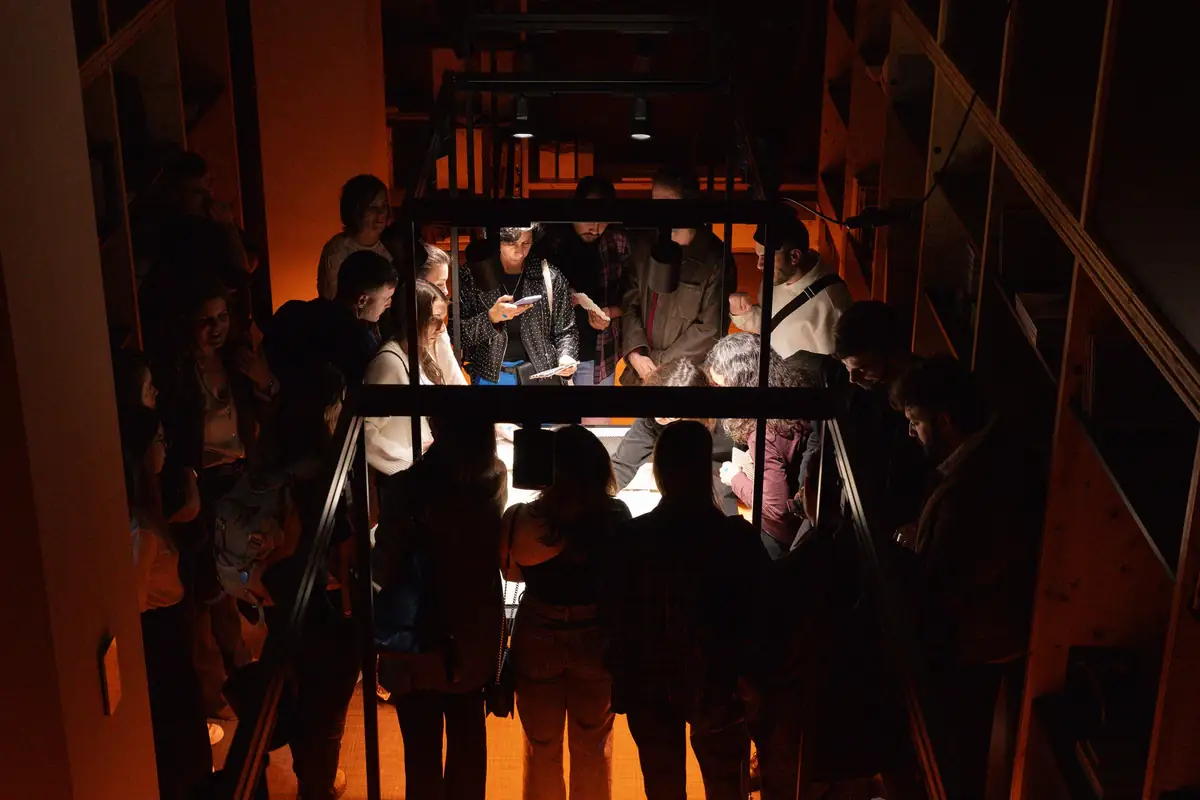 Asistentes alrededor de una mesa de materiales iluminada con luz cálida en un espacio en penumbra