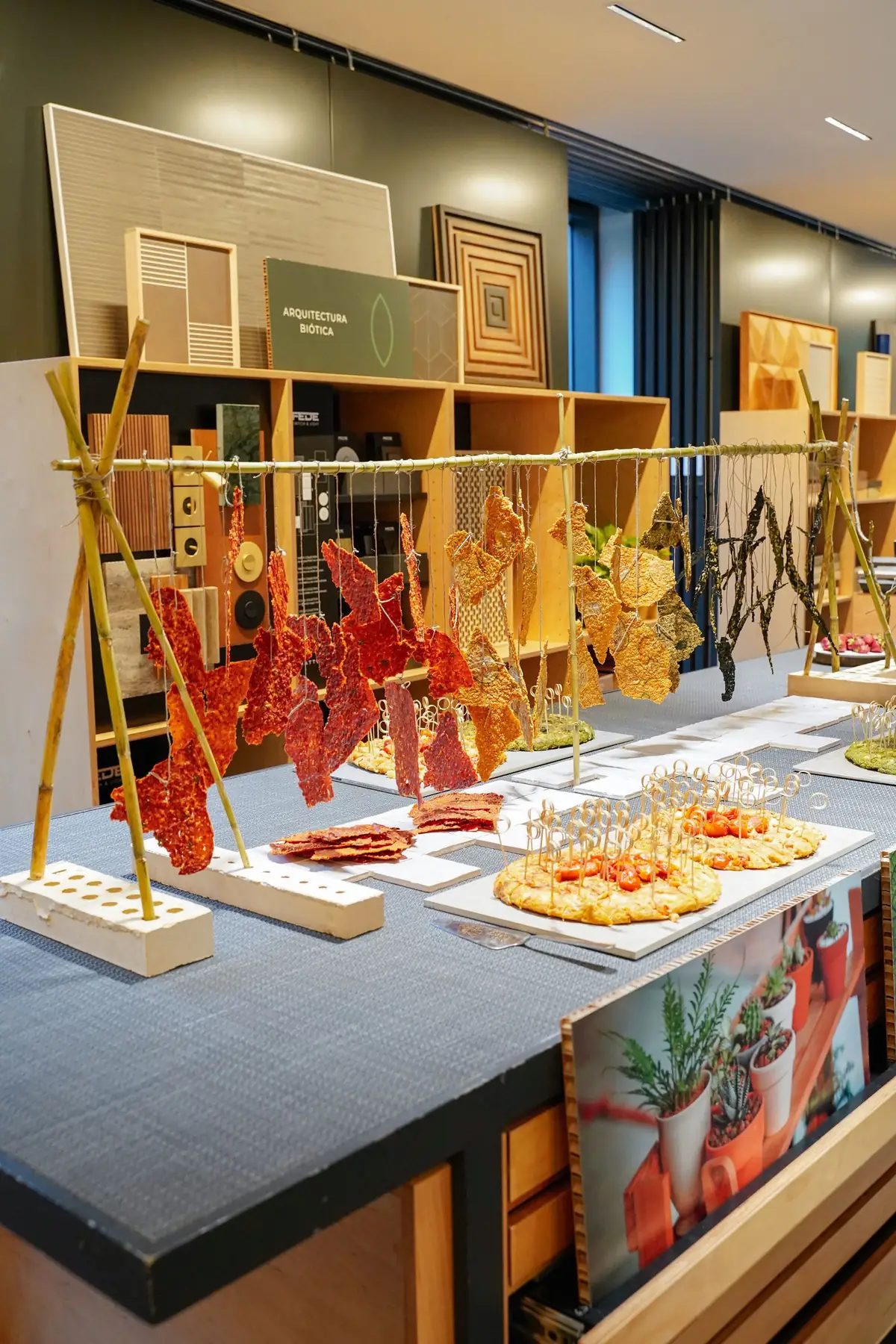 Mesa con láminas vegetales colgadas de una estructura de cañas, junto a muestras de materiales