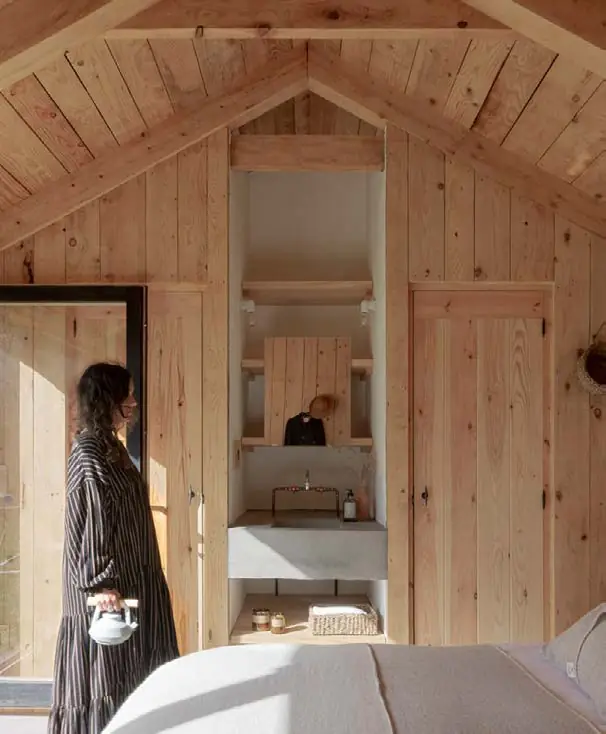 Dormitorio abuhardillado revestido de madera con el baño integrado al fondo