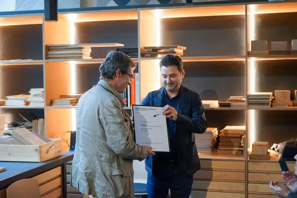 Un hombre entrega un diploma enmarcado a otro ante las estanterías de Matter