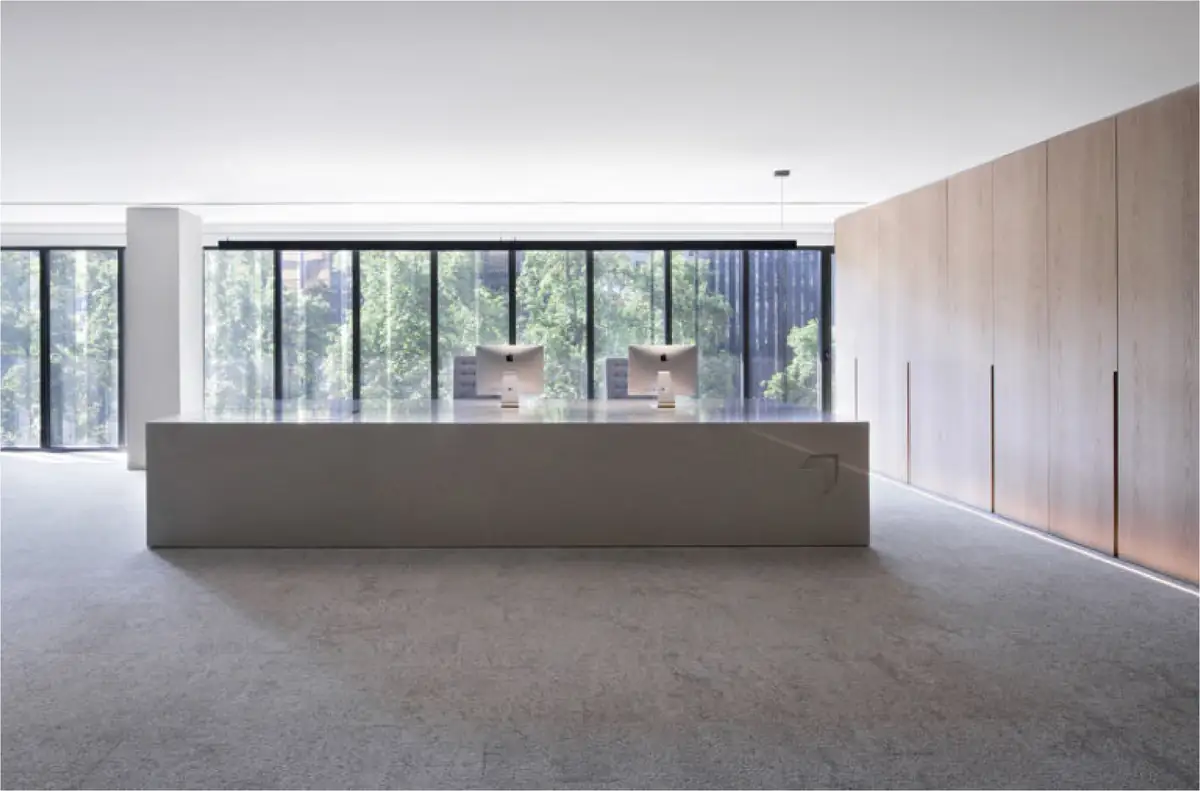 Recepción de oficinas con un gran mostrador blanco, armarios de madera y fachada acristalada hacia los árboles
