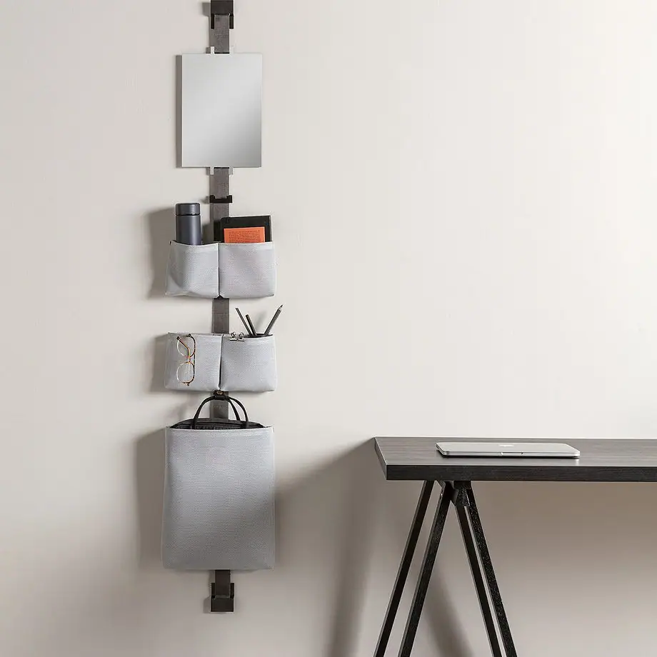 Banda TAPE STORAGE en la pared de un estudio, con espejo rectangular, bolsas grises y una bolsa grande junto a una mesa de trabajo