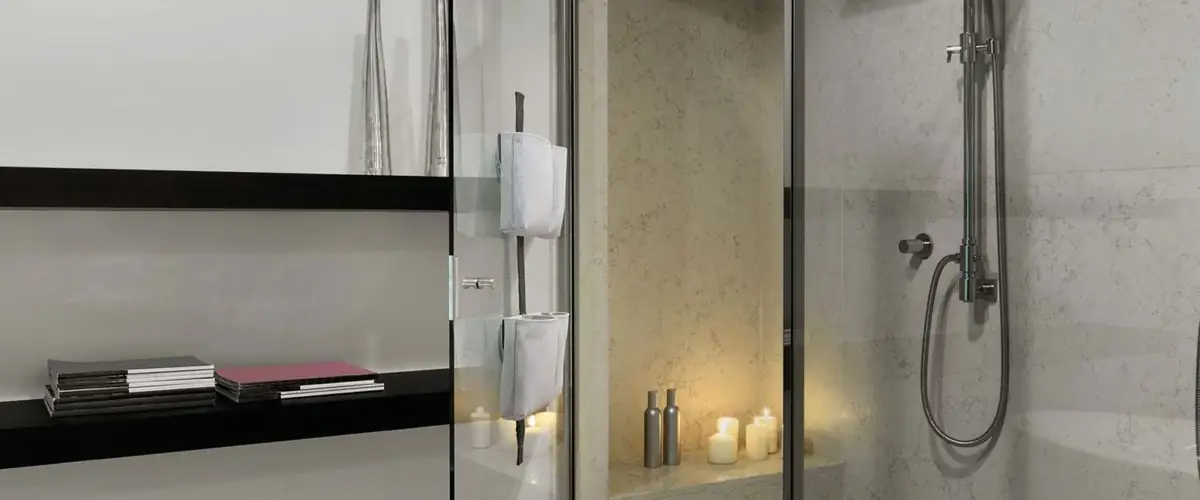 Ducha con mampara de vidrio y banda TAPE SHOWER con bolsas grises, junto a una repisa negra y velas