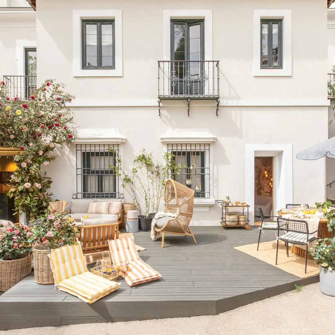Terraza de una casa blanca con tarima exterior gris, sillones de fibra y tumbonas a rayas