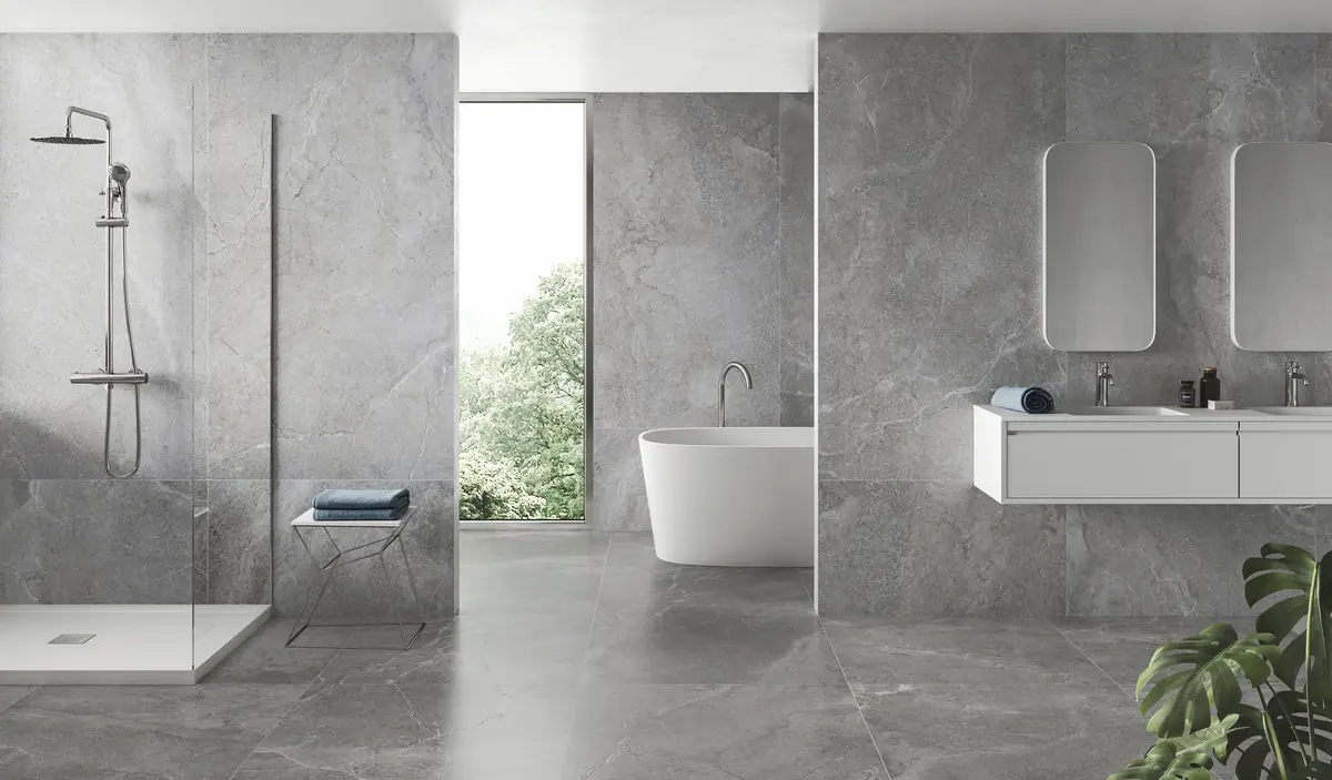 Baño con paredes y pavimento de porcelánico gris efecto piedra veteada en gran formato, ducha abierta y bañera exenta