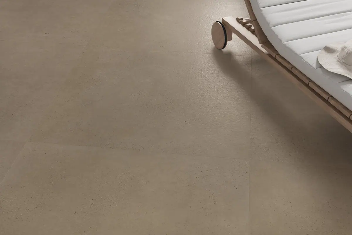 Pavimento de porcelánico efecto cemento en tono topo junto a una tumbona de madera