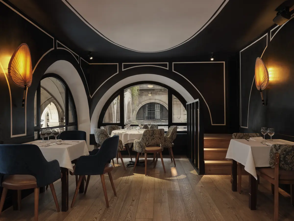 Comedor de paredes negras con molduras blancas y ventanales en arco, sillas tapizadas en terciopelo azul y en estampado paisley
