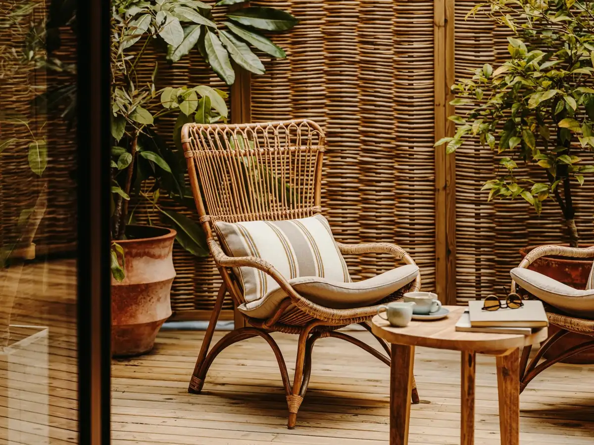 Butaca de ratán con cojín de rayas en una terraza con cerramiento de mimbre y plantas