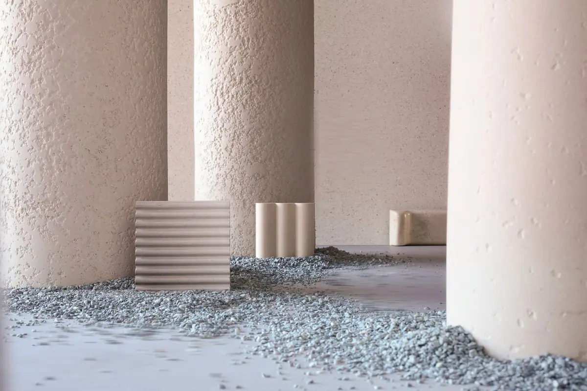 Columnas de textura cementicia y piezas acanaladas sobre un lecho de grava