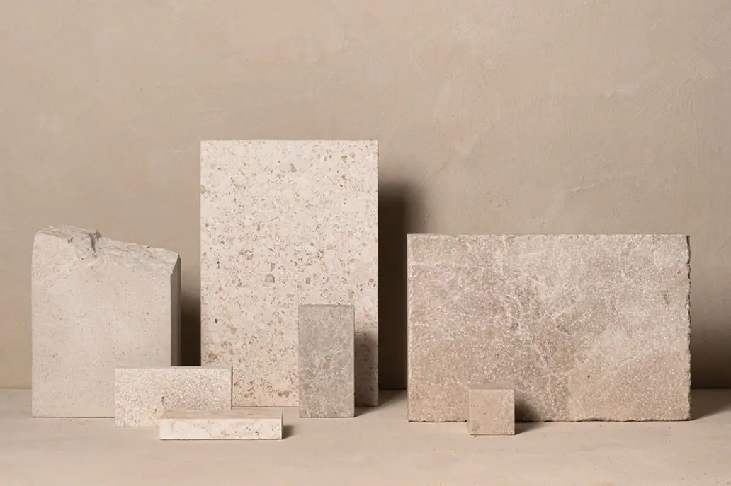 Piezas de piedra caliza clara de distintos formatos y acabados sobre una superficie beige