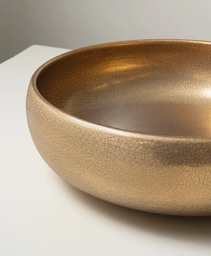 Lavabo de apoyo redondo con acabado dorado brillante y fino craquelado sobre una encimera blanca