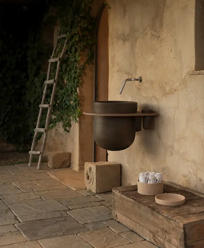 Lavabo suspendido de cerámica oscura con tablero claro fijado a un muro de piedra junto a una puerta