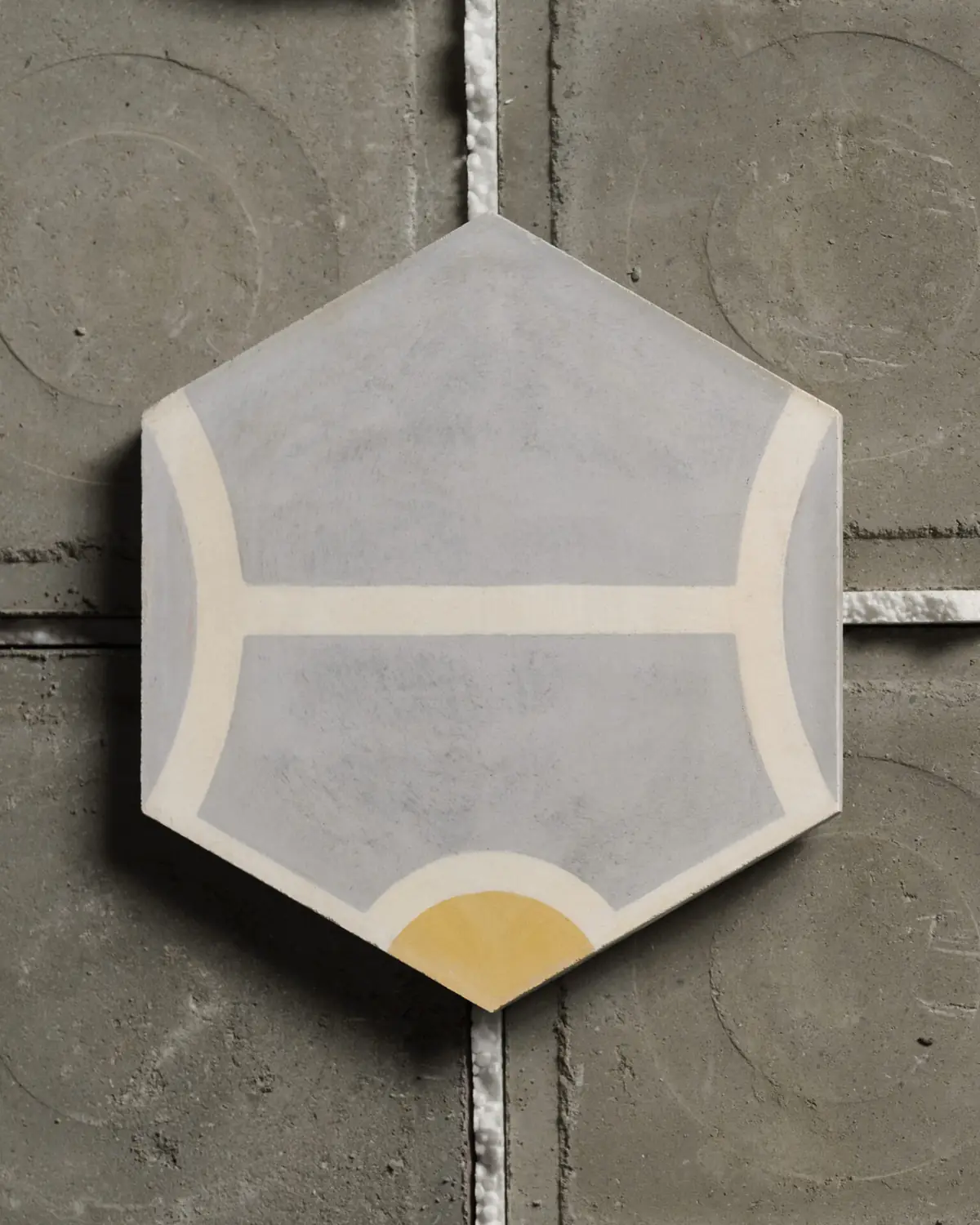 Baldosa hexagonal de cementina gris con líneas blancas y un semicírculo amarillo sobre un fondo de cemento