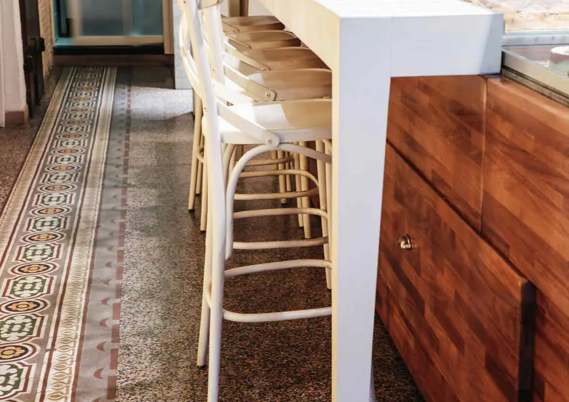 Pavimento de graniglia con una cenefa decorada junto a una barra con taburetes blancos