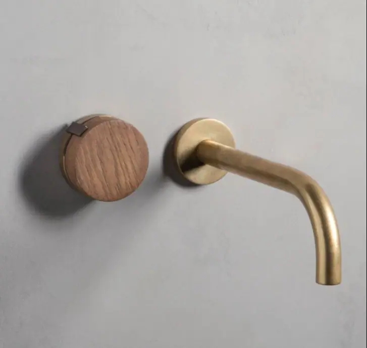 Grifo de lavabo mural con caño curvo de latón y mando redondo con tapa de madera sobre una pared gris
