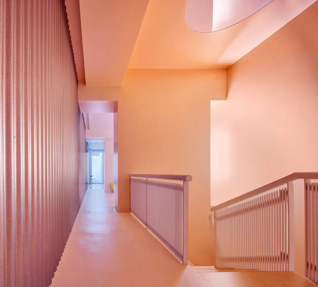 Rellano de la escalera en tonos rosa y naranja, con barandillas de lamas, chapa ondulada y un lucernario oval