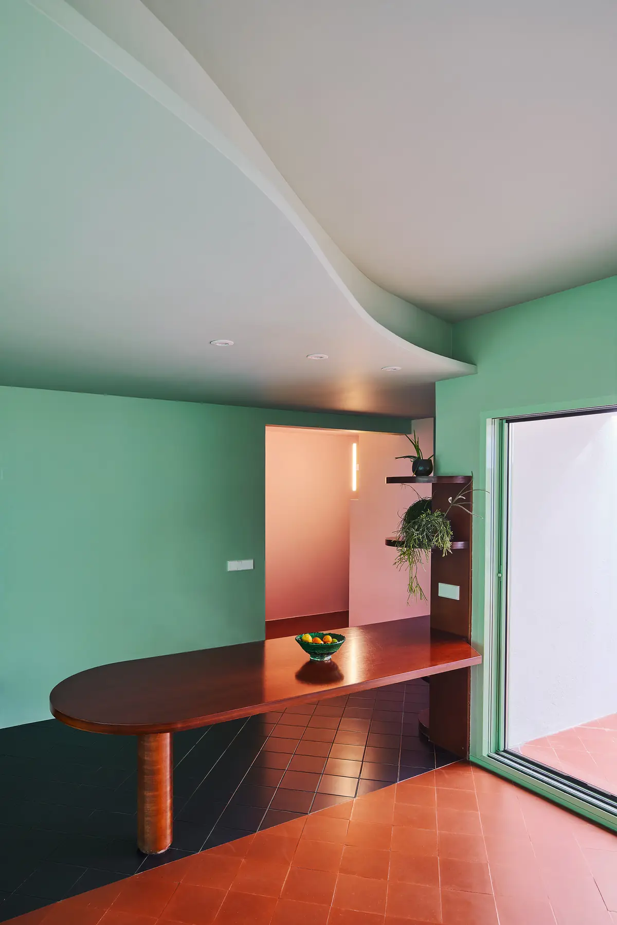 Estancia con paredes verdes, mesa de madera y encuentro entre pavimento negro y pavimento color teja