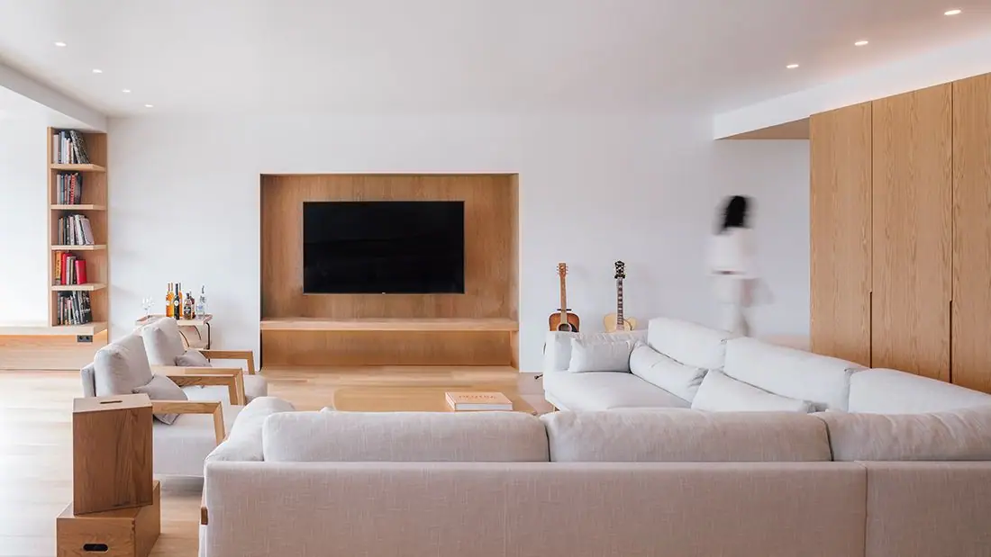 Salón con sofás blancos, mueble de televisión empotrado en roble y armarios de madera