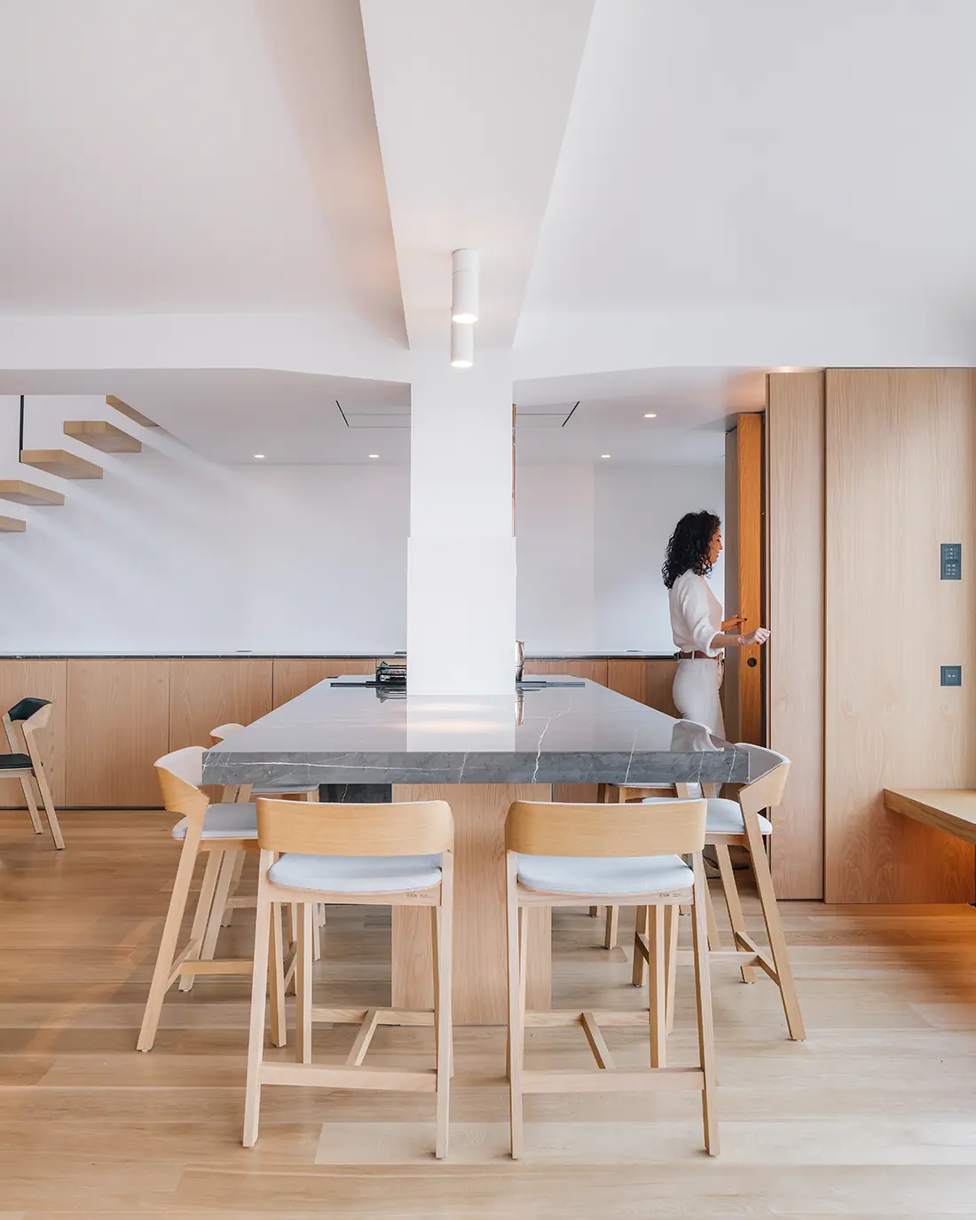 Isla de cocina con encimera de piedra y taburetes de madera, con armarios de roble al fondo