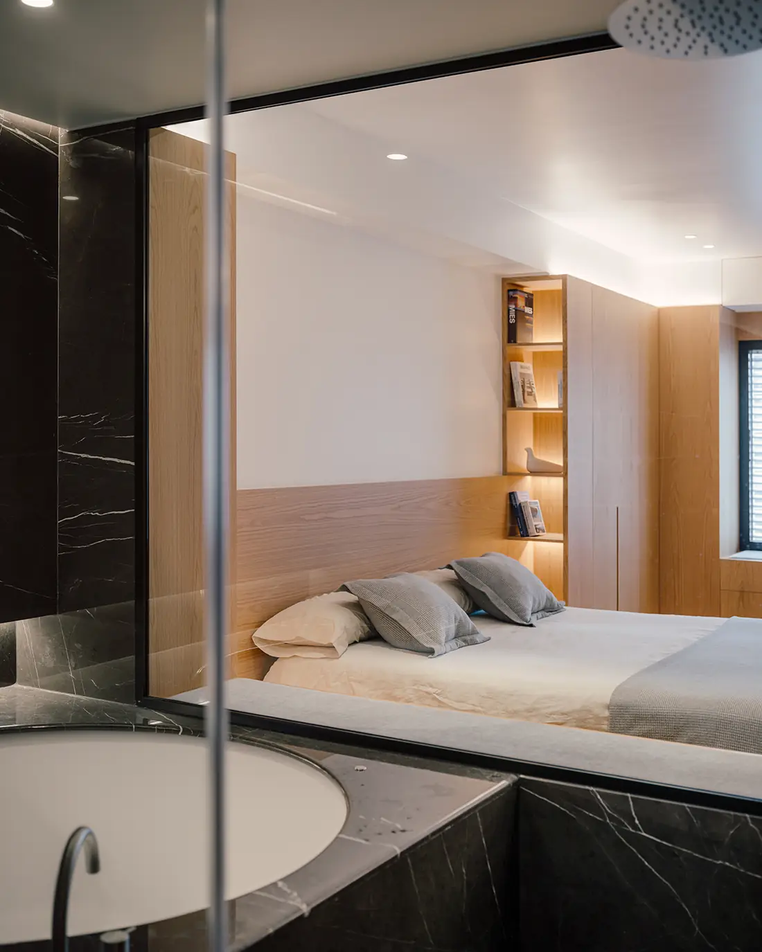 Bañera revestida de mármol negro separada del dormitorio por un cerramiento de vidrio