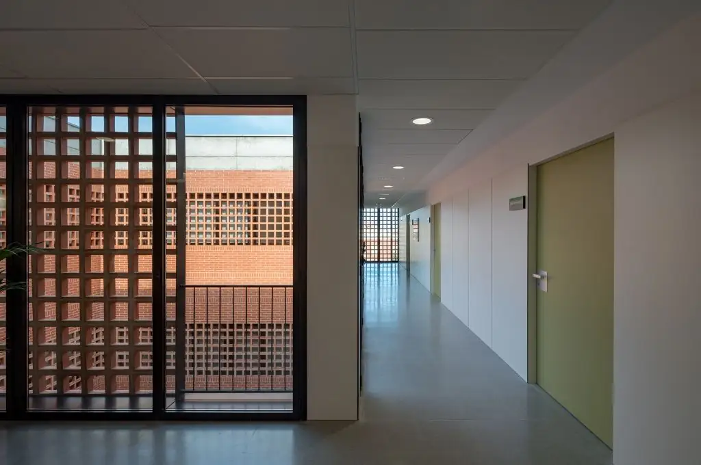 Pasillo blanco con puertas de consulta y, a la izquierda, un ventanal con celosía cerámica hacia el patio