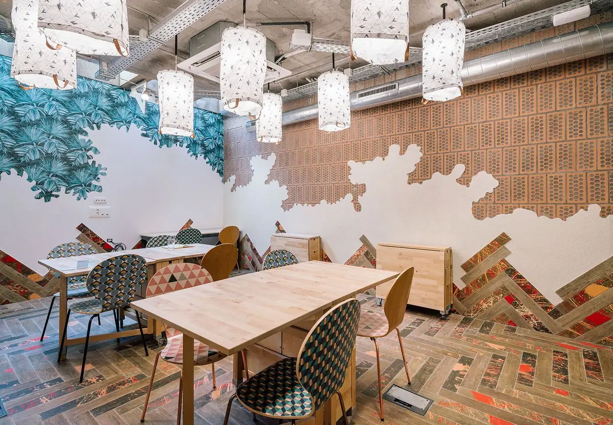 Sala de reuniones con lámparas de papel, mural de hojas, ladrillo perforado visto y pavimento en espiga salpicado de color