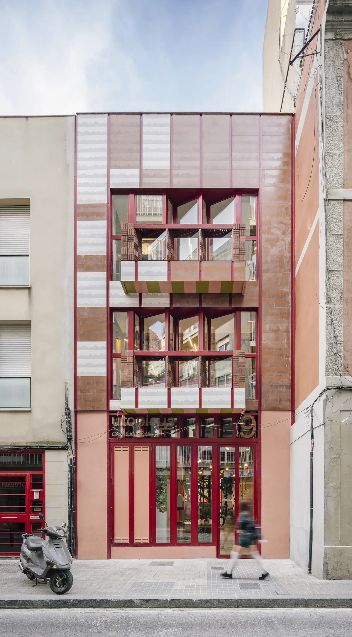 Fachada a la calle del Coworking Clementina, con piezas cerámicas en tonos terracota y blanco y carpinterías rojas