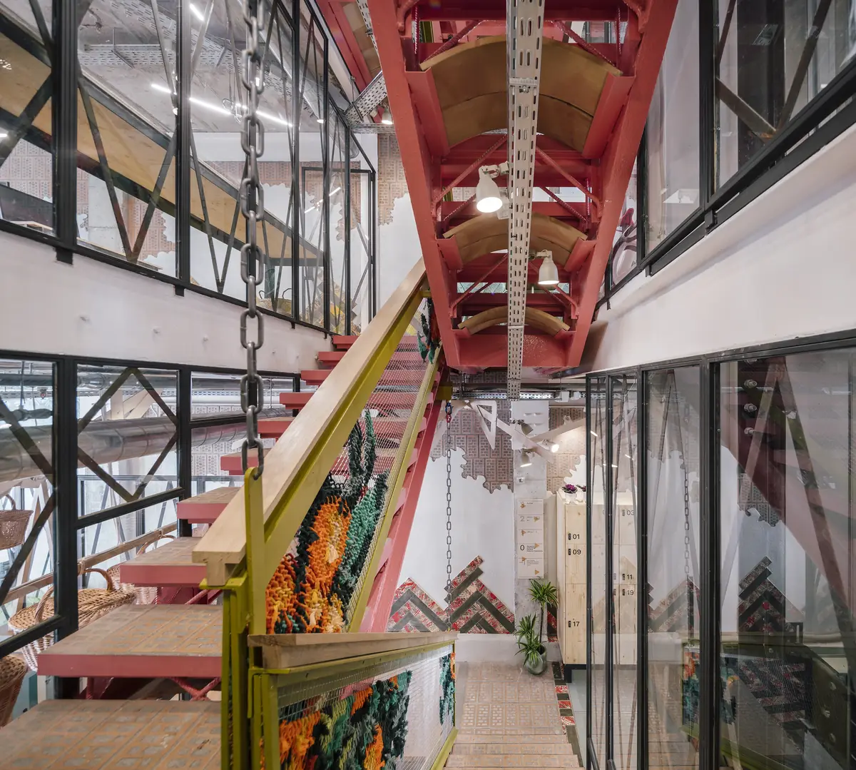 Escalera central de estructura roja vista desde abajo, entre salas acristaladas, con barandilla bordada