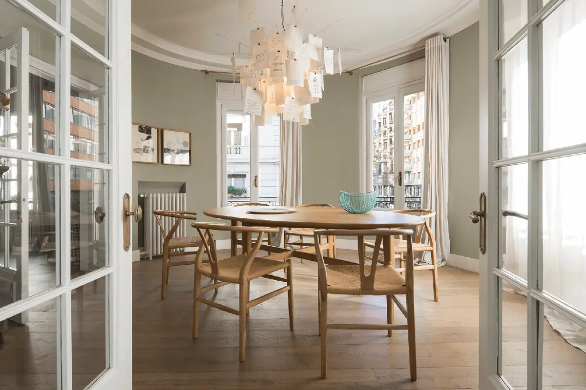 Comedor con mesa redonda de madera, sillas de madera y fibra natural y lámpara de papel, visto a través de puertas vidrieras