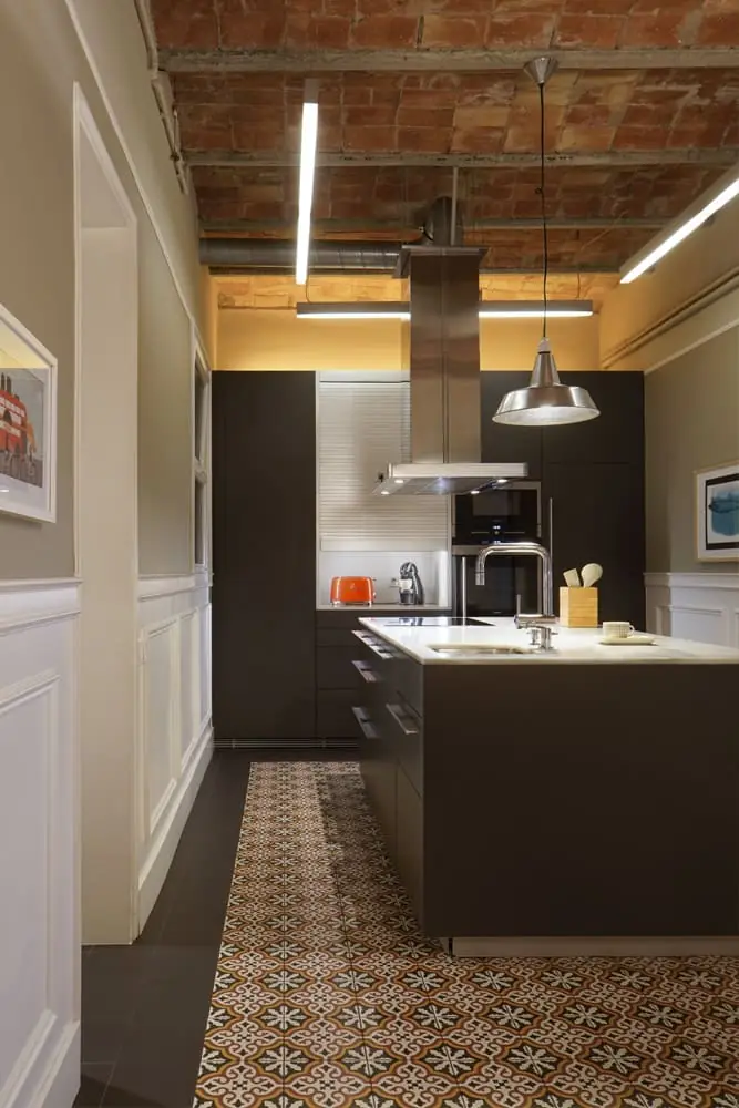 Cocina con isla oscura y encimera blanca, techo de bovedillas de ladrillo visto y pavimento de baldosa con dibujo