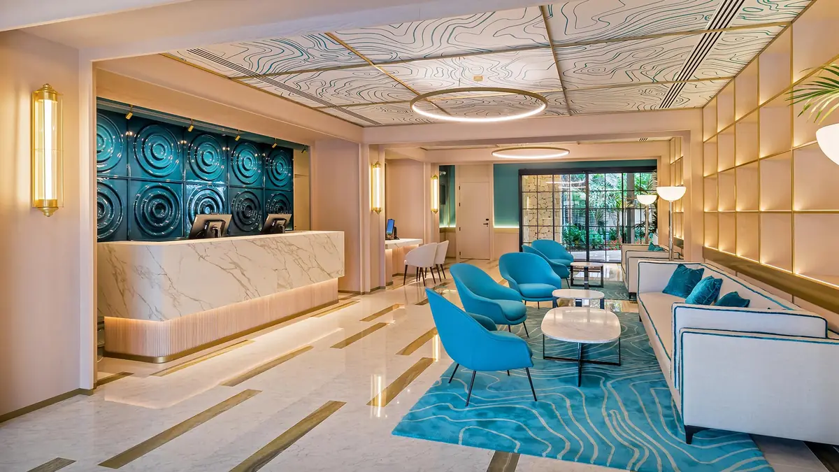 Recepción del hotel con mostrador de mármol, mural cerámico azul y alfombra con dibujo de olas