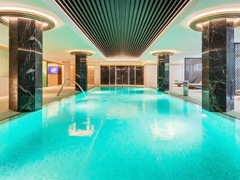 Piscina interior del spa con techo de lamas, columnas de piedra oscura veteada y gresite turquesa