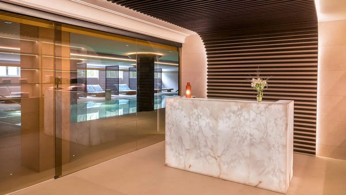 Recepción del spa con mostrador de alabastro retroiluminado, cerramiento de vidrio y pared de lamas
