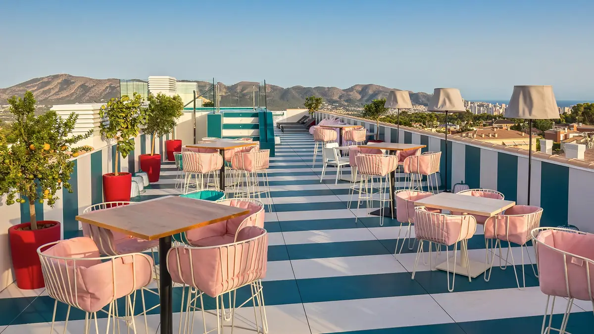 Terraza en cubierta con suelo a rayas blancas y azules, sillas rosas, limoneros y vistas a la sierra y al mar