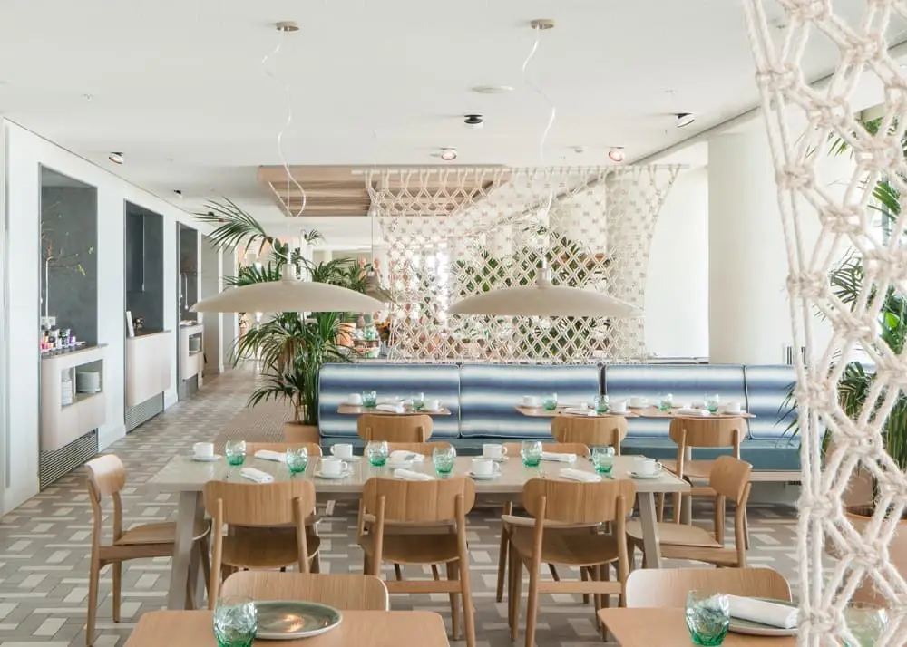 Comedor del restaurante con mesas de madera, banco tapizado a rayas y mamparas de macramé