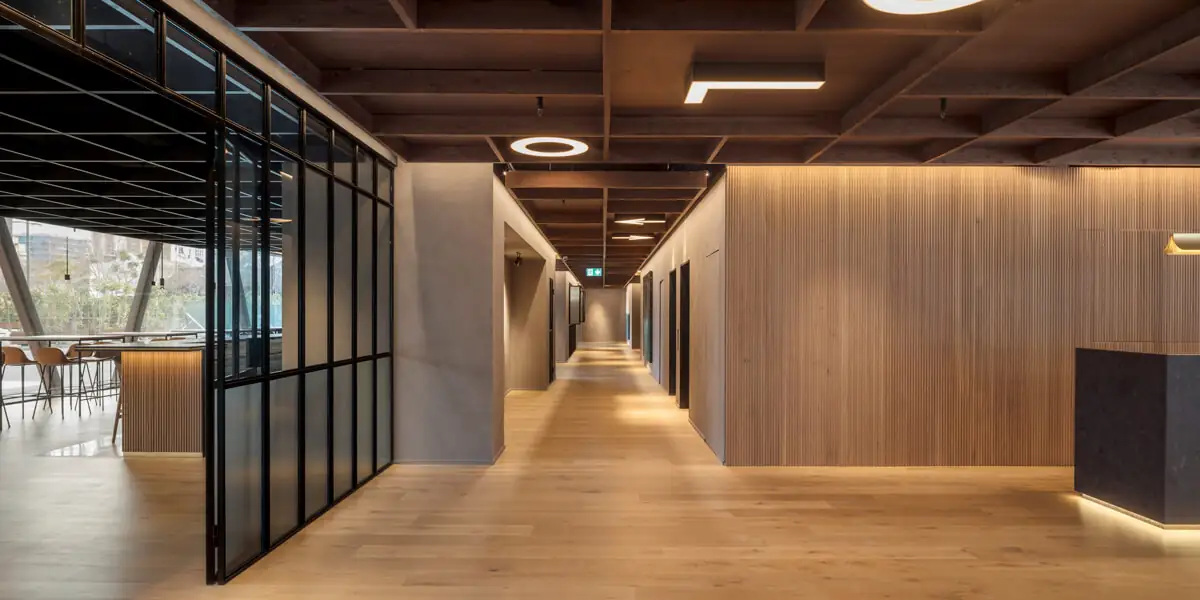 Pasillo de planta baja con paredes de listones de madera, techo de casetones oscuros y mampara de vidrio y perfilería negra