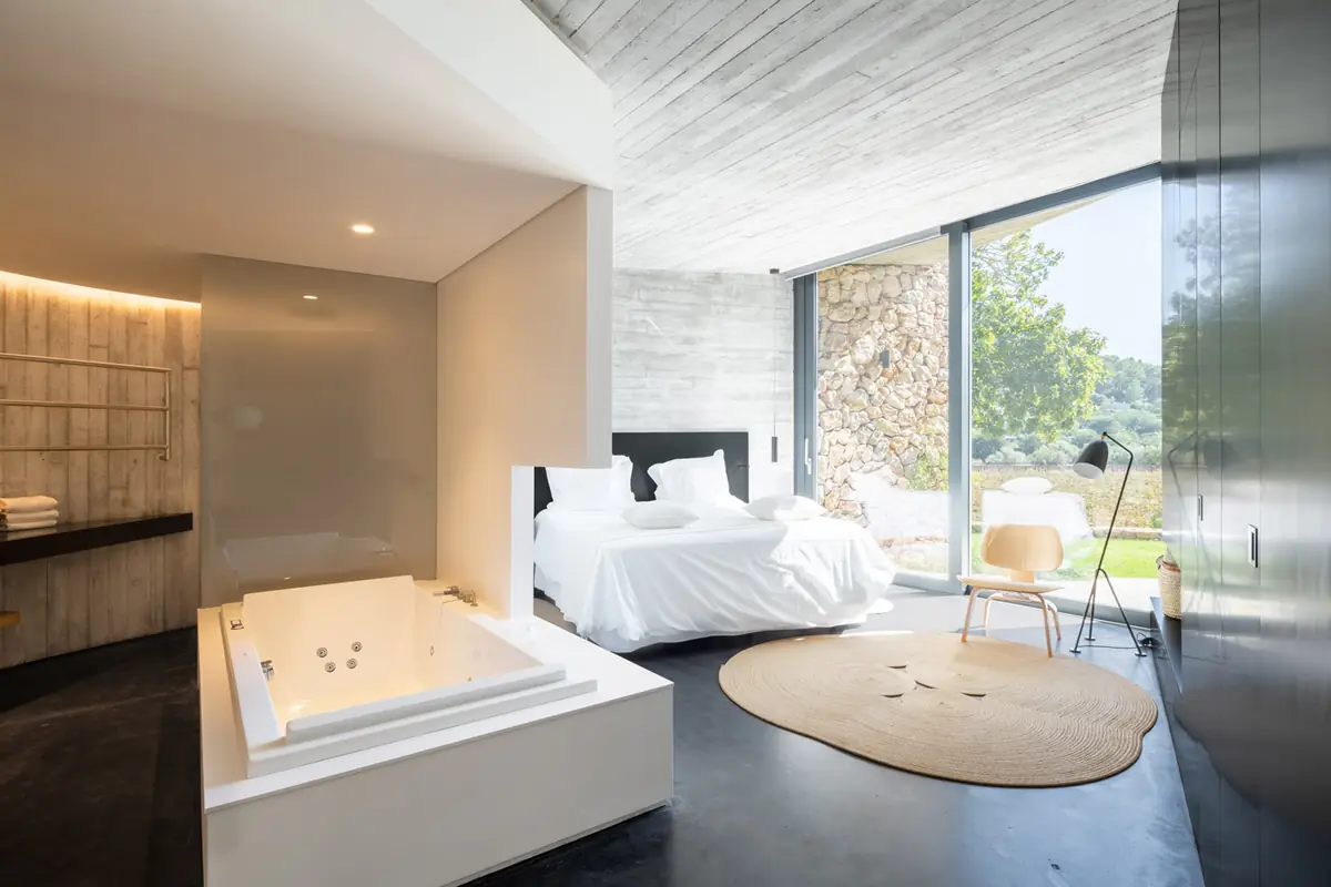 Dormitorio de una villa con bañera de hidromasaje, hormigón visto y ventanal al jardín
