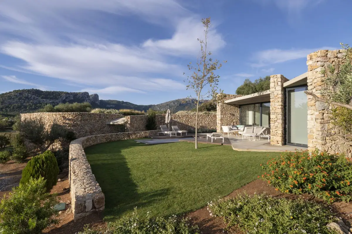 Jardín de una villa con muro curvo de piedra seca y fachada acristalada