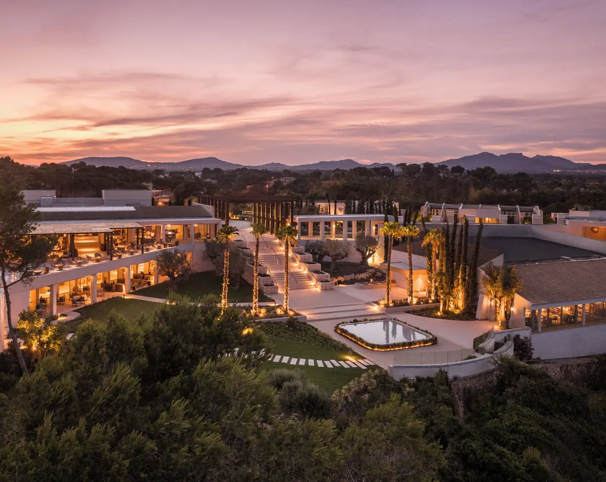 Vista del resort al atardecer con edificios bajos escalonados entre pinos y jardines