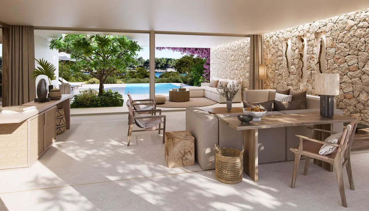 Salón de una villa con muro de piedra, sofás claros y terraza abierta a la piscina