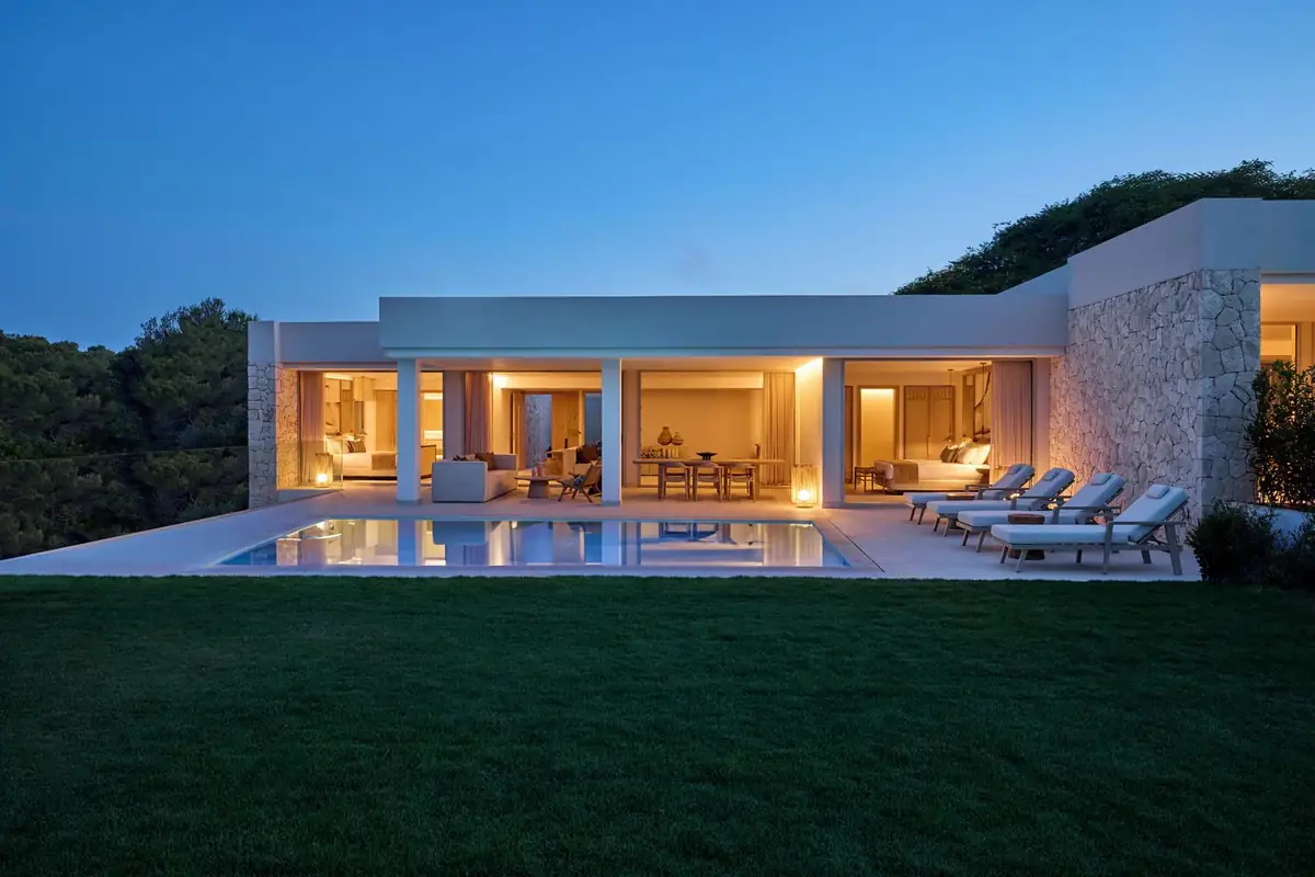 Bungalow de una planta con fachada acristalada, muro de piedra, piscina privada y césped al anochecer