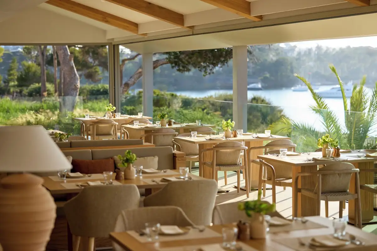 Comedor acristalado con mesas de madera y vistas a la cala y a los barcos