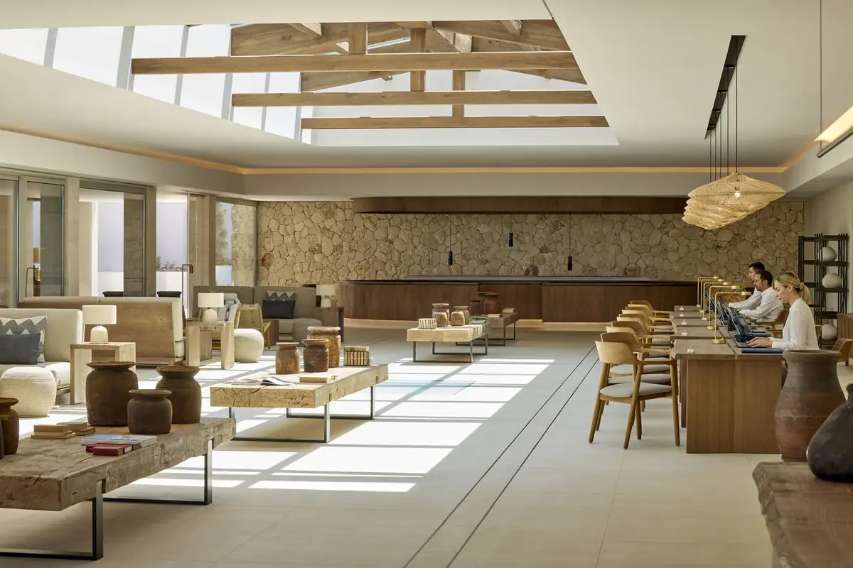 Lobby con lucernario, vigas de madera, muro de piedra y mesas bajas de madera maciza